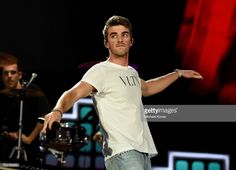 a man in white shirt and jeans standing on stage with his arms out to the side