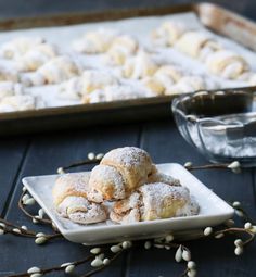 powdered sugar covered pastries on a plate next to a baking pan and glass dish