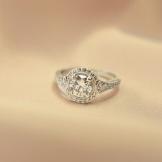 an engagement ring with a diamond center surrounded by white gold and pave diamonds on a beige background