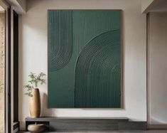 a large green painting hanging on the wall next to a vase with a plant in it