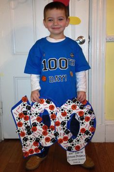 a young boy is standing in front of a door holding two large letters that say 100