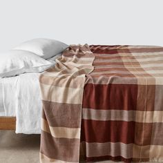 a bed with a plaid blanket on top of it next to a white pillow and pillows