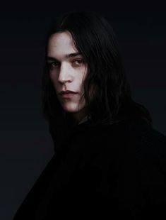 a man with long hair wearing a black sweater and dark background is looking at the camera