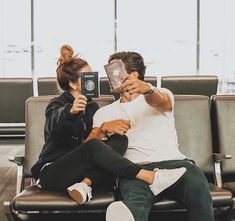 a man and woman sitting on a bench in an airport holding up their passports