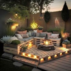 an outdoor seating area with wooden pallets and lights on the ground, surrounded by plants