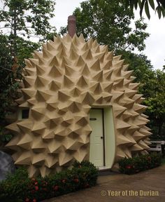 an unusual house made out of paper is in the middle of a garden with trees and flowers