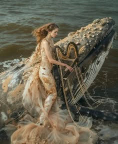 a woman in a long dress is holding a harp while standing in the ocean water