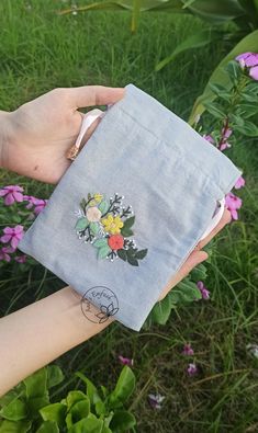 a person holding onto a small bag with flowers on it in front of some purple flowers