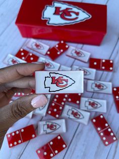 a hand is holding up a red and white domino board with the kansas chiefs logo on it