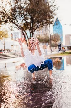 a woman in white shirt and blue jeans playing in water