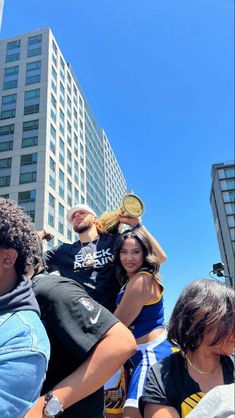 a group of people standing around each other in the middle of a street with tall buildings behind them