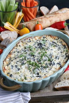 a blue dish filled with cheese and vegetables on a cutting board next to bread, tomatoes, carrots, celery