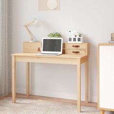 a laptop computer sitting on top of a wooden desk next to a white dresser and lamp