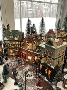 christmas village displayed in front of window with snow on ground and lit up trees outside