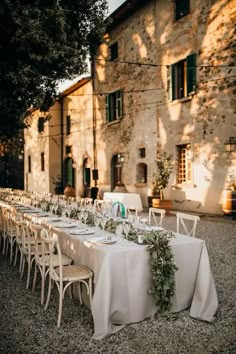 a long table with white linens and greenery sits in front of an old stone building