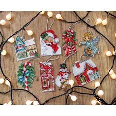 christmas ornaments are hanging on a wooden table with lights around them and some decorations in the shape of santa's house