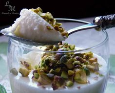 a spoon with some food in it on top of a glass bowl filled with yogurt and nuts