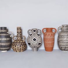 five vases are lined up on a shelf in front of the wall, one is painted black and white