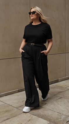 A black T-shirt tucked into tailored high-waisted trousers creates a timeless workwear look that’s both smart and comfortable. The monochromatic styling is perfect for the office or any formal setting, while white sneakers and subtle silver accessories add a touch of modernity to this effortlessly chic outfit. Spring 2025 Fashion Trends Plus Size, Midsize Work Fashion, Outfits To Hide Tummies, Mid Size Corporate Outfits, Spring Office Outfits Women Plus Size, Plus Size Summer Office Outfits, Office Outfit With Sneakers, Business Casual Outfits For Plus Women, Plus Size Smart Casual Outfits