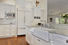 a large kitchen with white cabinets and marble counter tops, along with hardwood floorsing