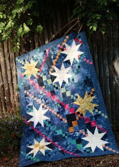 a blue quilt with stars on it sitting in front of a fence and some bushes