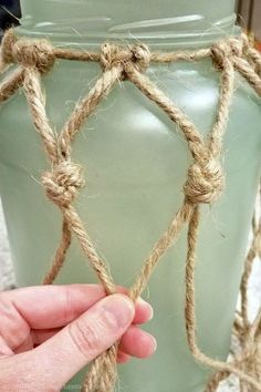 a hand is holding rope around a green vase with a knot on the top and bottom