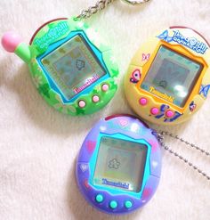 three electronic toys sitting next to each other on a white surface and one has a keychain