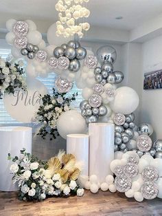 white and silver balloons are hanging from the ceiling in front of a table with flowers