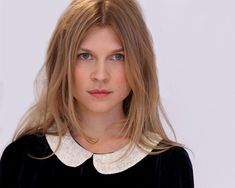 a woman with long blonde hair wearing a black top and white collared shirt is looking at the camera