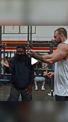 two men in a gym with one holding his arm out and the other pointing at him