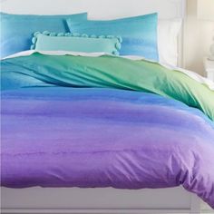 a bed with purple and green comforters on top of it next to a night stand