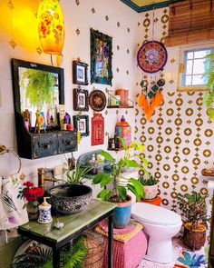 a bathroom with lots of plants and pictures on the wall above the toilet, along with other decorations