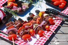 several skewers of meat and vegetables on a picnic table with red checkered cloth