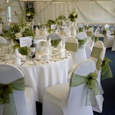 the tables are set up with white chairs and green sashes for guests to sit at