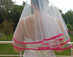 the back of a bride's dress with a pink ribbon on her belt and veil