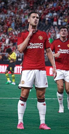 a man standing on top of a soccer field holding his hand to his mouth while wearing a red shirt