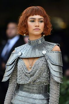 a woman with red hair wearing a silver dress and chain mailers on her shoulders