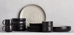 a stack of black cups and plates sitting on top of a white countertop next to each other