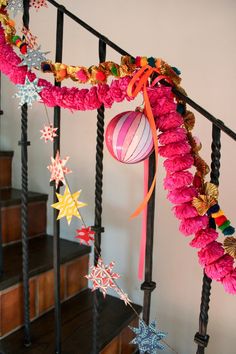 a staircase decorated with pink and gold garland, ornaments and stars hanging from the banister