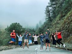 a group of people jumping in the air on a road with trees and fog behind them