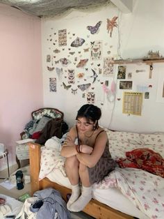 a woman sitting on top of a bed in a room filled with clothes and clutter