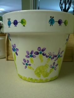 a white flower pot sitting on top of a counter next to a planter filled with purple and green flowers