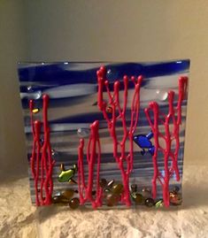 a blue and white glass block with red corals on the bottom, fish in the water