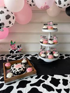 a table topped with cupcakes and cake next to pink and black balloons in the shape of cows