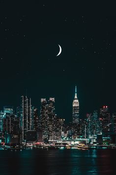 the city skyline is lit up at night, with a crescent moon in the sky