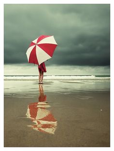 a woman standing on the beach holding an umbrella with a quote above her that reads, having courage does not mean that we are unafraid