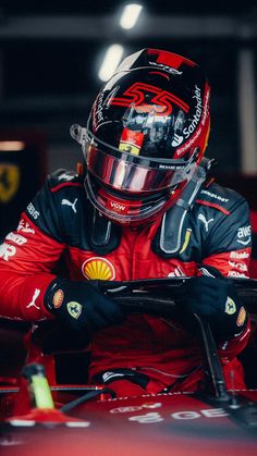 a man in a red racing suit and helmet sitting on top of a race car