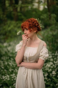 a woman with red hair wearing a white dress and holding a flower in her mouth