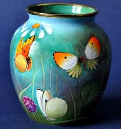 a blue vase with butterflies painted on the side and flowers in the bottom, sitting on a blue surface