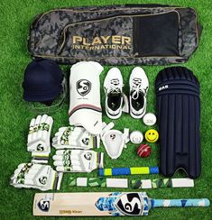 the contents of a cricket kit laid out on green grass, including bat, gloves and ball